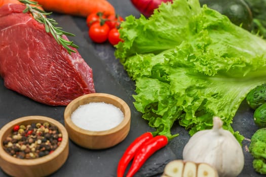 Red beef steak with a sprig of rosemary lies surrounded by spices: vegetables and herbs. The concept of proper and healthy nutrition, diet, menu, natural and organic products. High quality photo