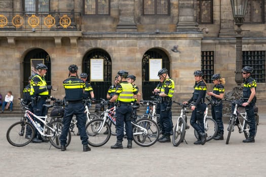 AMSTERDAM, THE NETHERLANDS - APRIL 16, 2019: Uniformed police officers on bicycles wearing helmets maintain order. Surveillance in the center of the city.
