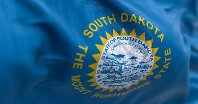 Close-up of the South Dakota flag waving in the wind. Sky blue field, the state seal, and inscriptions of South Dakota and The mount rushmore state. 3d illustration render. Selective focus