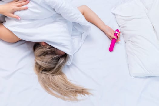 Woman in bed under sheets holding vibrator in hand. High quality photo