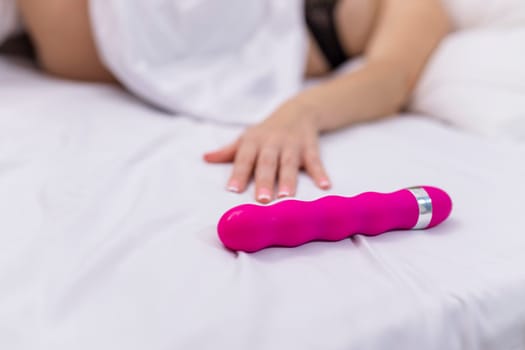 Woman in bed under sheets holding vibrator in hand. High quality photo