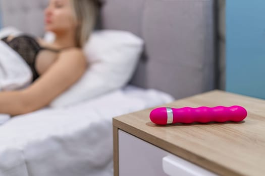Young woman holding sex toy dildo vibrator in bed.