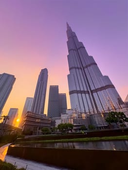 UAE, Dubai, 26 December 2024: The famous Burj Khalifa skyscraper at dusk, Dubai's sights during the incredible sunset sky, skyscrapers illuminated at night, pink sky, palm trees. High quality photo