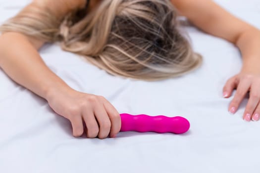 Woman in bed under sheets holding vibrator in hand. High quality photo