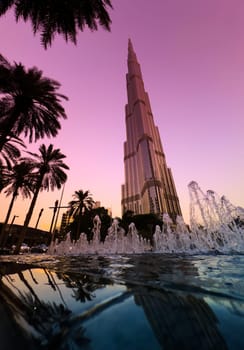 UAE, Dubai, 10 December 2024: The famous Burj Khalifa skyscraper at dusk, Dubai's sights during the incredible sunset sky, skyscrapers illuminated at night, pink sky, palm trees. High quality photo