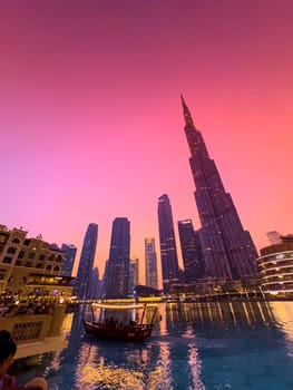 UAE, Dubai, 26 December 2024: The famous Burj Khalifa skyscraper at dusk, Dubai's sights during the incredible sunset sky, skyscrapers illuminated at night, pink sky, palm trees. High quality photo