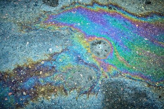 Spilled gasoline creating an abstract stain on the asphalt, highlighting the effects of motor oil on the surface