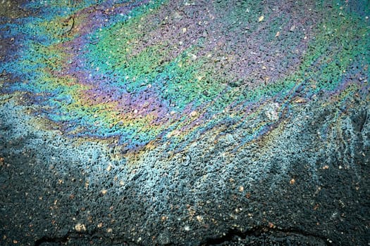 Petrol spill on asphalt creating a textured abstract design, showcasing the colors of motor oil and gas