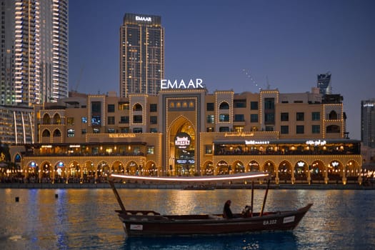 UAE, Dubai, 11 December 2024: A traditional tourist boat abra with tourists on the water waiting for the famous dancing fountain show in Dubai next to the mall at evening, people on embankment. High quality photo