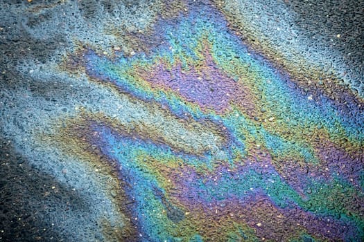Abstract design formed by an oil spill on the asphalt, featuring stains from gas or petrol