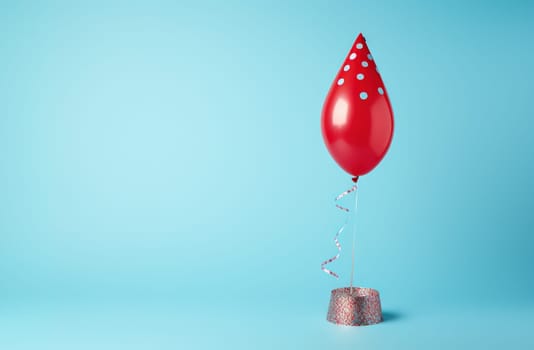 Red birthday balloon wearing cone carnival hat for celebration with confetti on the blue background. Generated AI