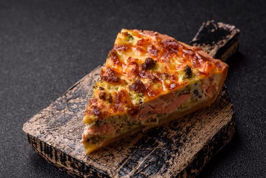 Delicious fresh quiche with broccoli, cheese, spices and herbs cut into pieces on a dark concrete background