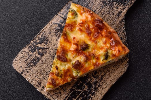 Delicious fresh quiche with broccoli, cheese, spices and herbs cut into pieces on a dark concrete background