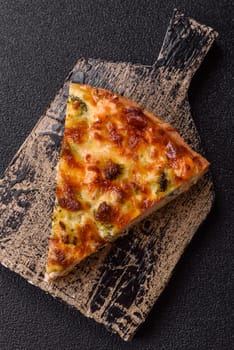 Delicious fresh quiche with broccoli, cheese, spices and herbs cut into pieces on a dark concrete background