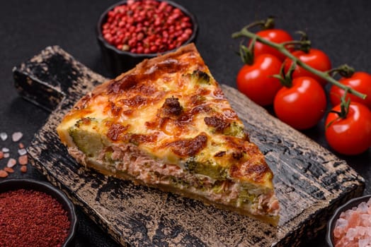 Delicious fresh quiche with broccoli, cheese, spices and herbs cut into pieces on a dark concrete background