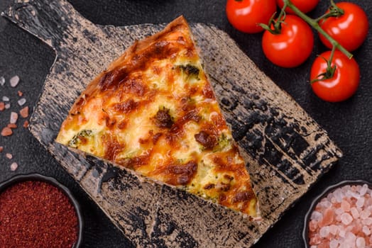 Delicious fresh quiche with broccoli, cheese, spices and herbs cut into pieces on a dark concrete background