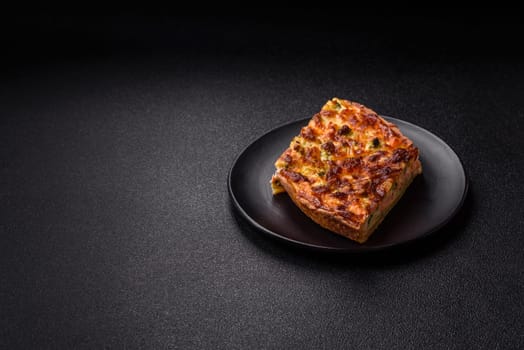 Delicious fresh quiche with broccoli, cheese, spices and herbs cut into pieces on a dark concrete background
