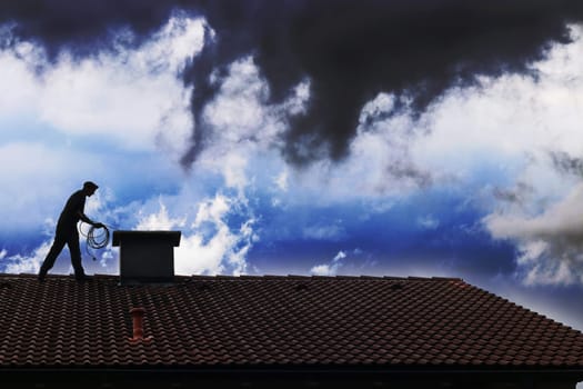 Ein Kaminkehrer säubert auf einem Hausdach den Kamin vor einer dramatischen Himmelsstimmung