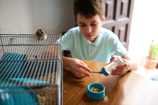 A young boy sits at a table, attending to his pet hamster and its water bottle. The hamster is perched on its cage, creating a lively and wholesome domestic scene showcasing care and responsibility.