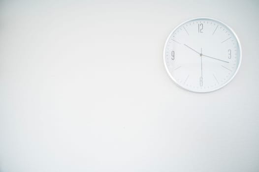 white round clock on a white wall. the clock is located in the upper right part. space for an inscription. the clock shows 10.18