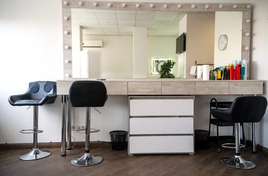 Makeup artist and hairdresser's office. Modern furnishings. High black leather chairs for clients and a large rectangular mirror. Beauty salon with modern furniture