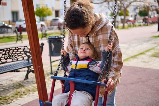 A joyful moment of a mother gently helping her young child swing in a vibrant park, fostering connection and happiness.