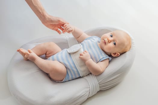 Adorable 3-month-old baby lying safely in a cozy infant cocoon secured with a special safety belt. Comfortable and protective design for newborn care. Parenting, safety, and baby comfort concept.