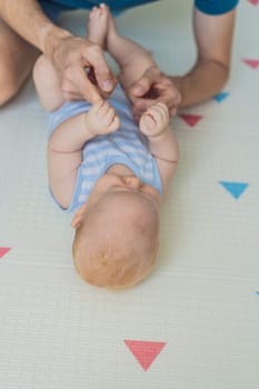 A baby lies on a soft children play mat while their father hands gently support and protect them. Heartwarming moment of care and connection. Parenthood, safety, and love concept.