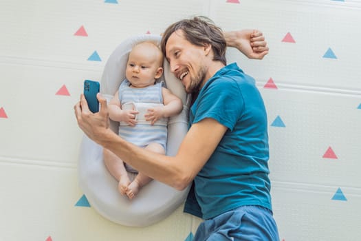 A 3-month-old baby lies safely in a cozy infant cocoon, secured with a special safety belt, while their father lies beside them during a video call. Modern parenting, bonding, and technology concept.