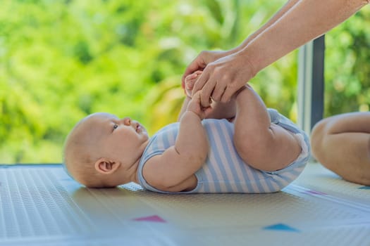 A mother practices baby gymnastics with her 3-month-old on a soft children's play mat. A joyful and nurturing moment focused on bonding, development, and care. Early childhood, fitness, and parenting concept.