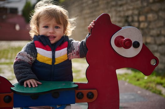 A cheerful toddler enjoying their time outside while playing on a large playground toy shaped like a horse. The sunny day highlights the child's joyful expression and the vibrant colors of the equipment.