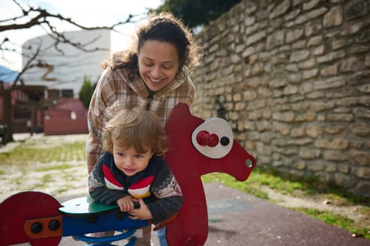 A happy mother and child engaging in playful activity on a colorful playground spring toy outdoors.