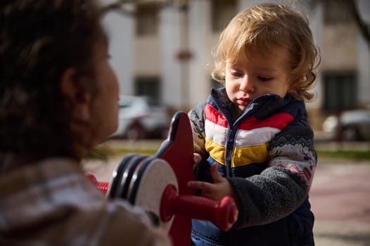A young child is exploring and interacting with playground equipment outdoors, accompanied by a caring adult. Captures an intimate moment portraying childhood curiosity and family bonding in a park environment.