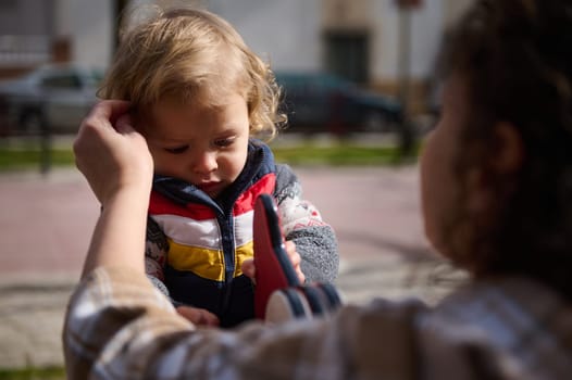A scene depicting a mother aiding her child, showcasing care and love in an outdoor park setting on a clear, bright sunny day.