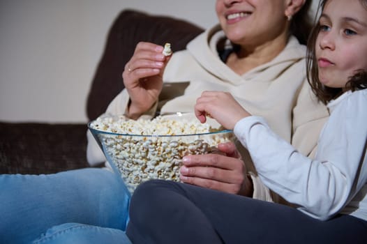 A smiling mother and her preteen daughter enjoy snacks and time together on a comfortable couch.
