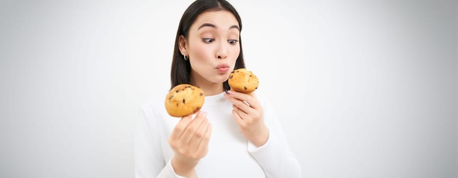 Close up portrait of asian girl eats cupcakes with happy face, isolated on white background.