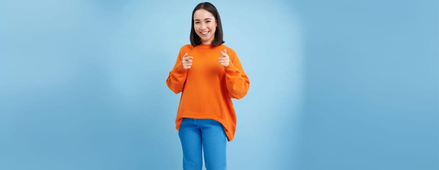 You got this, good job. Enthusiastic korean woman, points at camera with finger pistols and smiles, encourages, praises, stands over blue background.
