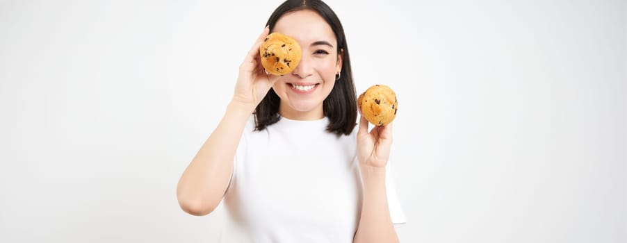 Close up portrait of smiling korean woman, shows tasty cupcakes, eating cake and looking happy, pastry and bakery concept.