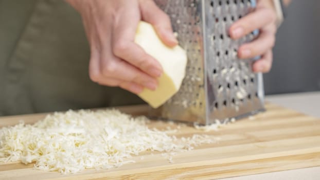chef grating traditional mozzarella cheese with steel grater on the wooden board.