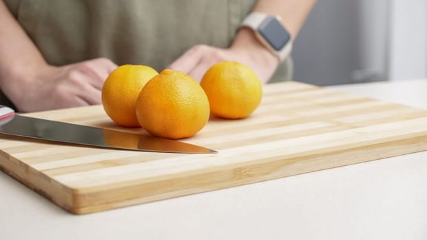 Hands cutting orange tangerines on the cutting board on table, lots of juicy fresh fruits for cooking.