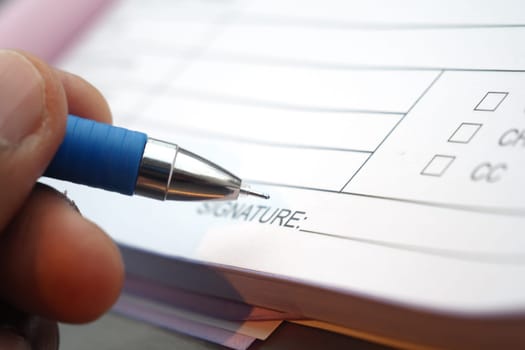 A hand is using a blue pen to sign a document with checkboxes.