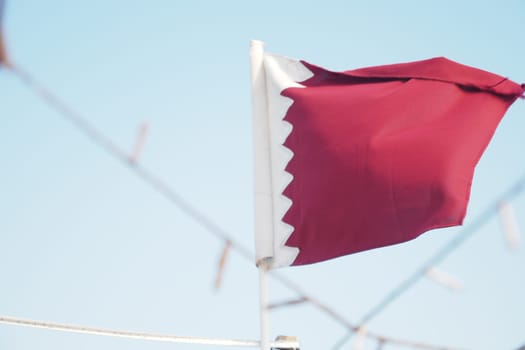 A vibrant flag of Qatar flutters in the breeze on a sunny day.