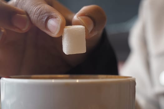 A hand gently places a sugar cube into a warm drink at a cafe.