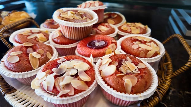 Delicately frosted cupcakes with almond slices await customers in a bakery.