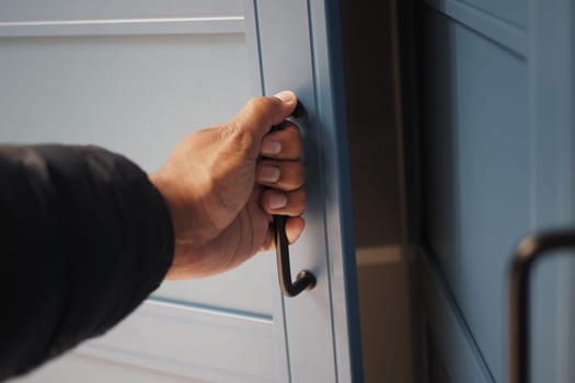 A person grips the handle of a blue cabinet door indoors, prepared to open it.