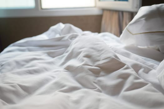 Crumpled white sheets lie on a cozy bed under warm sunlight.