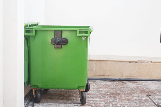 A green waste container stands next to a wall in a city area.