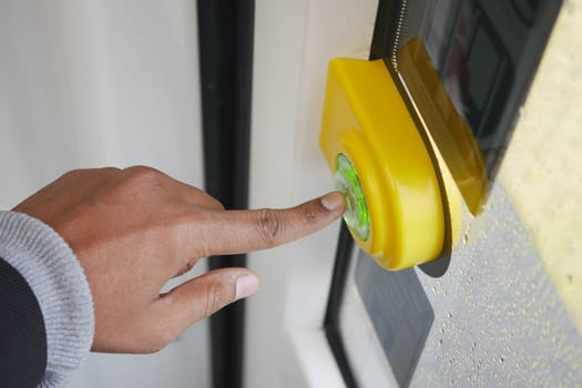 Individual activates a bright green bus stop button on a rainy day.