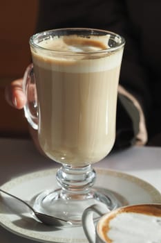 A person holds a glass of creamy coffee during a relaxing moment.