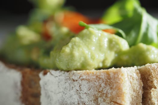 Avocado spread generously placed on whole grain bread with greens nearby.